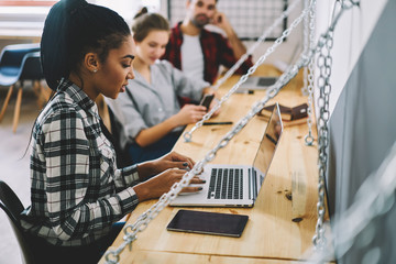 Good looking young it professional searching information in internet for personal website on modern laptop computer using wireless connection sitting in coworking interior after working process