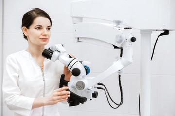 A beautiful and cute dentist in a white coat holds medical equipment in his hands and looks to the side.