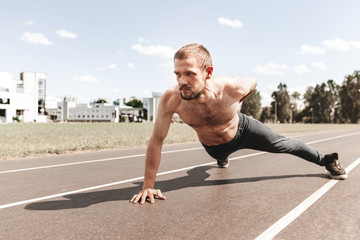 Portrait of a young man doing push-ups with one hand in the street