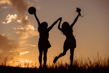 Two female silhouette figures jumping in the afternoon light.