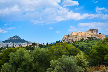 Fototapeta premium Iconic vew of Acropolis hill and Lycabettus hill in background in Athens, Greece from Pnyx hill in summer daylight with great clouds in blue sky.