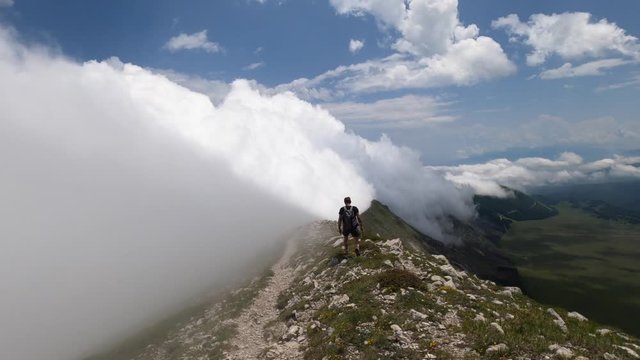 Man walking on the edge of a mountain, cloudscape moving with the wind over the mountain. Aerial view, 4k