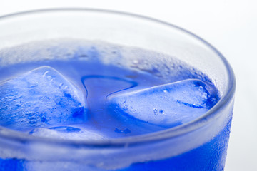 Bright glass refreshing beverage with melting ice cubes in blue alcohol syrop and condensation on its wall isolated white background macro