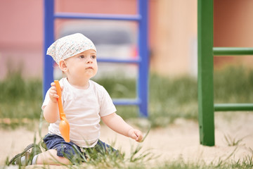 A small child sits on his knees in the sandbox in the playground.