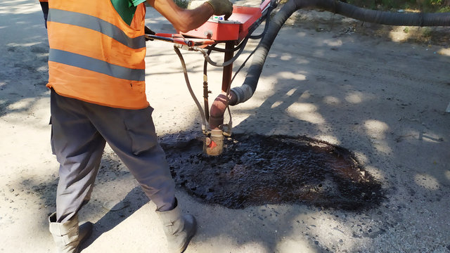 Worker patching up the road, repairing holes in the road.