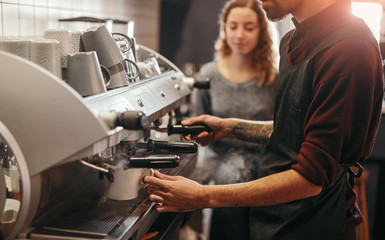 Barista with colleague making coffee in coffee machine
