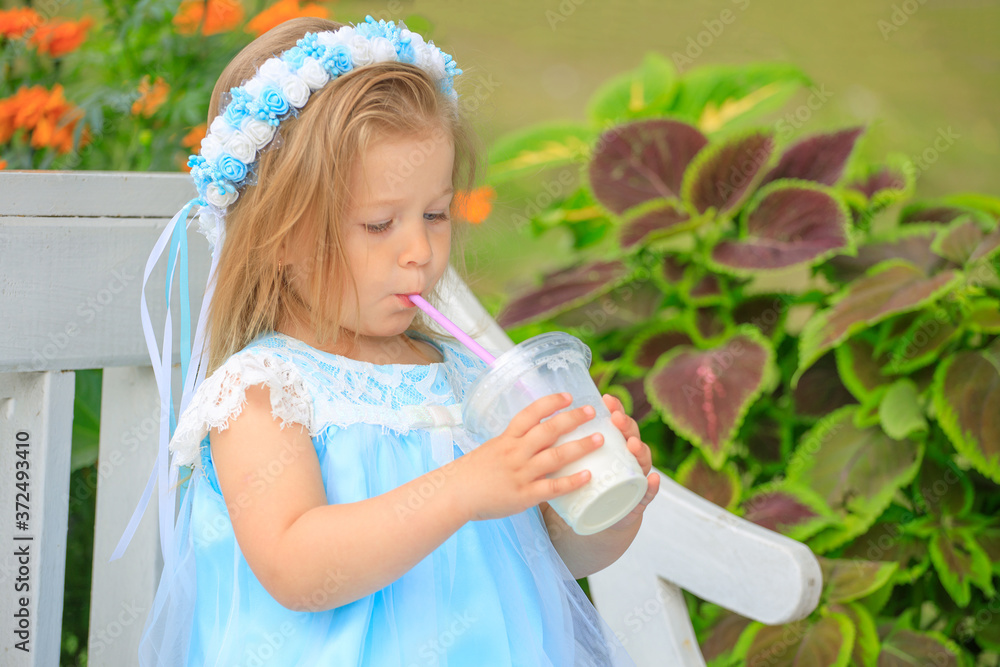 Canvas Prints little girl sits on a bench in a blue dress and drinks a milkshake