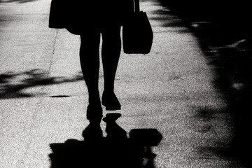 Silhouette and shadow of lonely woman walking on a street. Female legs on a sidewalk, concept of...