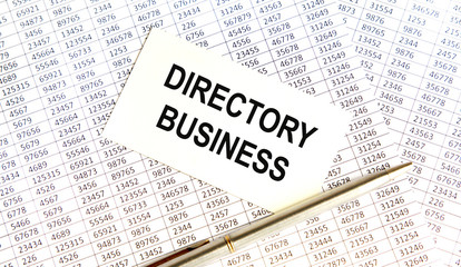 Obraz premium On the card is the inscription DIRECTORY BUSINESS, next to the pen, books in the background, business concept.