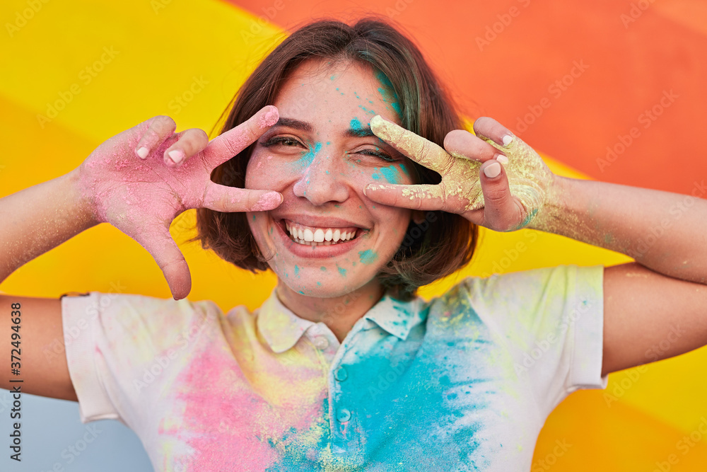 Wall mural Happy young woman gesturing V sign during paint festival