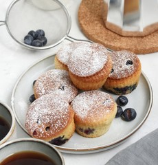 Muffins on a gray plate on a light table with a cup of coffee, blueberries and a coffee pot