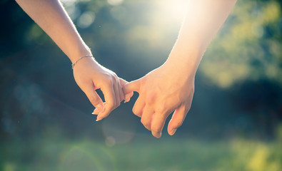 young couple holding hands at sunset, close-up detail of pinkies in sunlight, love and romance gesture or symbol