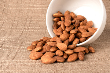 Almonds in a white bowl on a background on jute fabric. Best healthy food almond concept
