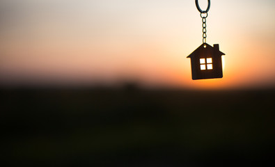 Silhouette of a house figure with a key, a pen with a keychain on the background of the sunset. They dream of a house, building, moving to a new house, mortgages, renting and buying real estate. Copy 