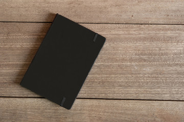 Blank Black Notebook with leather cover placed on wooden desk. Education and Business Mock up concept