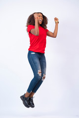 pretty young african woman wearing red top and blue jeans jumping with excitement and happiness