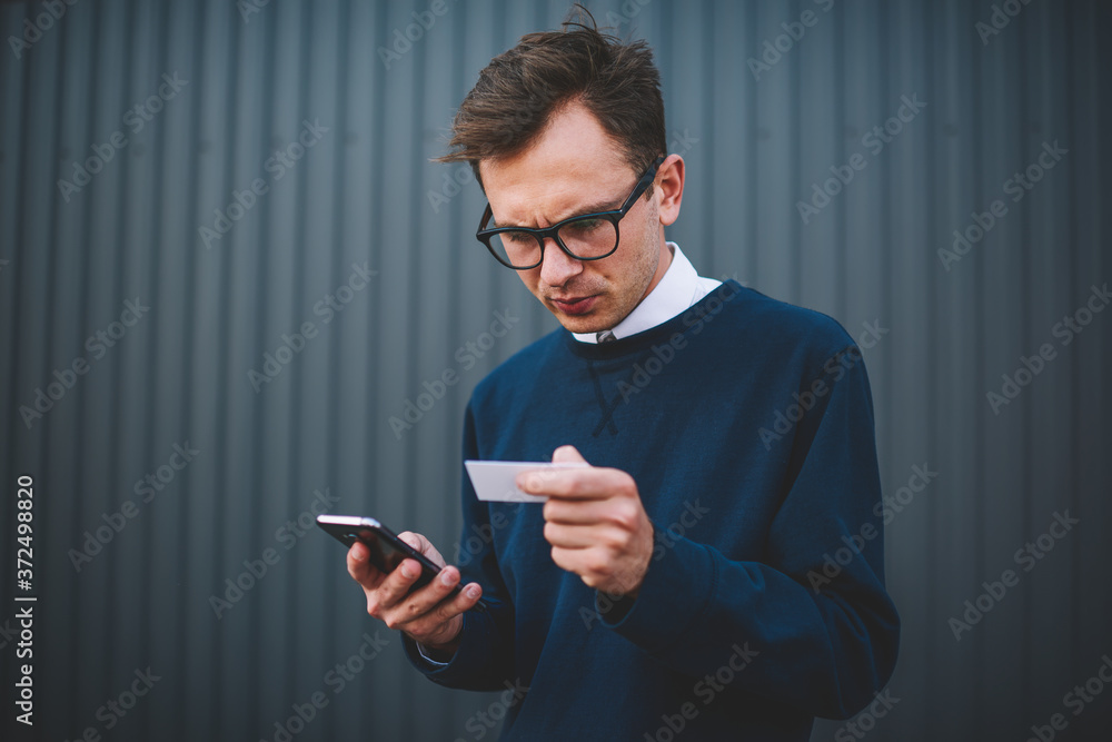 Poster handsome pensive male blogger dressed in stylish clothes checking visit card and searching informati