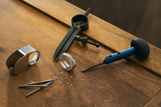 Workplace of a jeweler with tools and equipment for working on an old wooden table. Ready-made diamond engagement ring, diamonds, divider, magnifying glass. Engraver at work on jewelry from diamonds