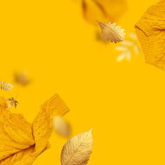 Frame made of orange flying women's knitted sweater and golden autumn leaves on yellow background....