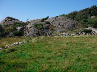 Landscape photo of three stone fences crossing each other in a field.  A rocky hill and blue sky is in the background