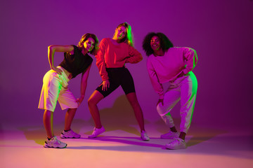 Fototapeta na wymiar Flexible. Sportive girls dancing hip-hop in stylish clothes on purple-pink background at dance hall in green neon light. Youth culture, movement, style and fashion, action. Fashionable portrait.