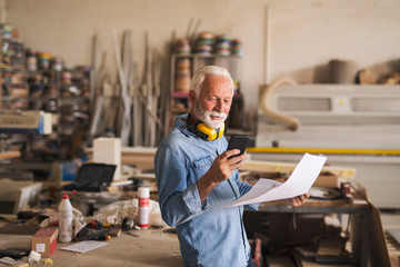 Senior woodworker in a good mood is casually looking at the cellphone