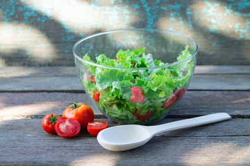 Healthy organic salad with fresh vegetables and herbs in glass bowl with wooden spoon on rustic table