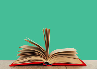 Open book textbook in a red cover on a wooden desk with mint green background. Back to school distance home education.Quarantine concept of stay home.