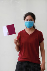 Masked woman in brown shirt and small Qatar flag in hand.