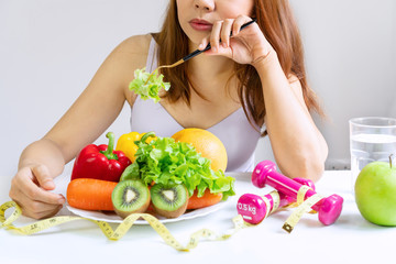 Obraz na płótnie Canvas Unhappy young Asian woman bored emotion on dieting time and refuse eating fresh green vegetables in fork on dining room at home, girl dislike taste of vegetable. Healthy food concept. Close up