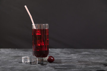 Cold cherry juice with ice in a glass with a straw stands on a black background. Copy spaes.