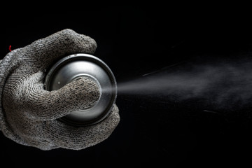 A hand in a glove holds a spray can on a black background. View from above.