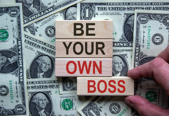 Wooden blocks form the words 'be your own boss' on beautiful background from dollar bills. Male...
