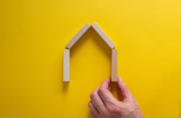 Fototapeta na wymiar Male hand builds a model of a wooden house from wooden blocks. Copy space. Business concept. Beautiful yellow background.