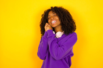 Dreamy young female with pleasant expression, closes eyes, keeps hands crossed near face, thinks about something pleasant, poses against gray background.