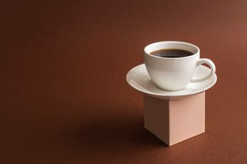 Cup of coffee on cube pedestal on brown