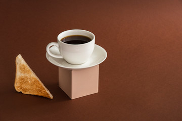 Cup of coffee on cube pedestal with toasts on brown