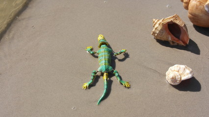 Green toy lizard on the shore of the lake.