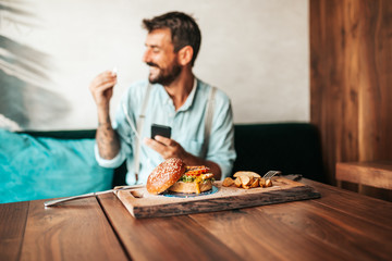 Handsome middle age man sitting in restaurant and enjoying in delicious burger.