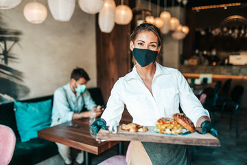 Beautiful young waitress with face protective mask serving delicious burger to middle age male...