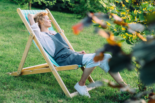 Beautiful blond slim graceful woman gardener relaxing in deckchair after working at garden outdoor.