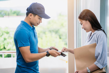 Asian deliveryman delivering package box parcel giving to female customer signing using smart...
