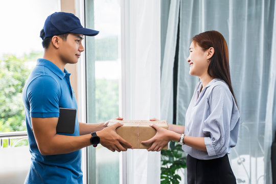 Asian deliveryman delivering package box parcel giving to female customer at home delivery service logistics business ordering mail posting business at front door of house wearing formal uniform