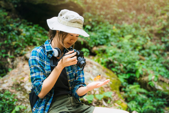 Asian girl traveler hiking traveling sitting on a rock taking picture of butterfly exploring jungle nature forest waterfall, wearing travel gear, summer hot healthy outdoor peaceful freedom lifestyle