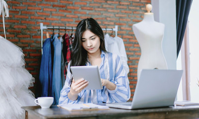 Asian beautiful woman fashion designer using tablet working cheering in success in video call with collogues discussing innovative ideas work planning strategy ecommerce during quarantine isolation