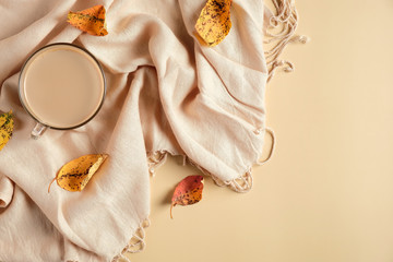 Flatlay autumn composition with cup of coffee, fallen leaves and scarf on beige background. Hygge style, cozy autumn workspace concept.