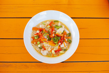 Bowl of chicken and vegetable soup on a very orange table