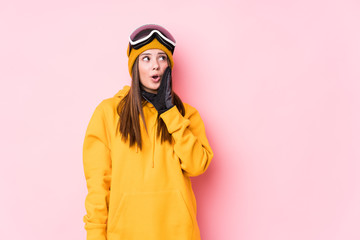 Young caucasian skier woman isolated is saying a secret hot braking news and looking aside