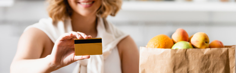 panoramic shot of woman holding credit card near paper bag with groceries