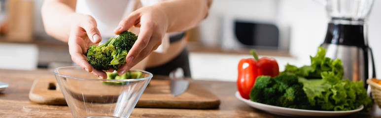 panoramic orientation of woman putting broccoli in bowl near vegetables